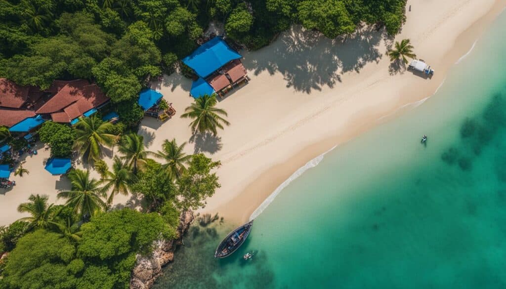 image from the sky of a Thai beach. This image is taken with a drone and shows a white/yellow beach, beautiful green water and some cabins.